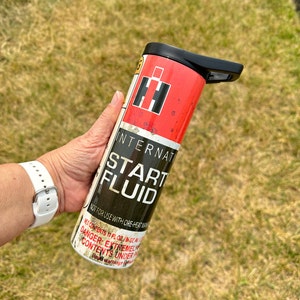 May include: A red and black stainless steel tumbler with a distressed look. The tumbler features the International Harvester logo and the text "Start Fluid" with the warning "Not for use with ore-heat manifolds".