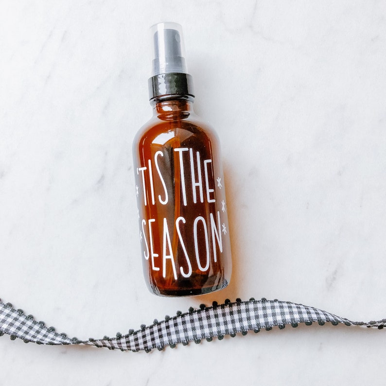 May include: A brown glass bottle with a black spray top and a white label that says "Tis the Season" with snowflakes.