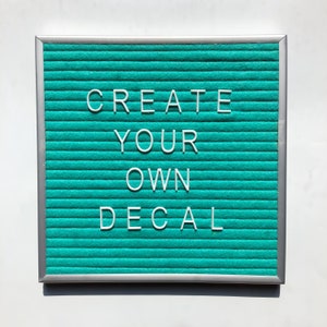 May include: A teal letter board with a silver frame displays the text "CREATE YOUR OWN DECAL".