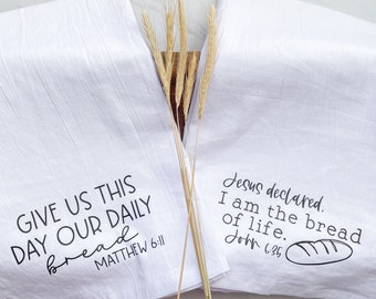May include: Two white kitchen towels with black text. The first towel says "Give us this day our daily bread Matthew 6:11". The second towel says "Jesus declared. I am the bread of life. John 6:35".