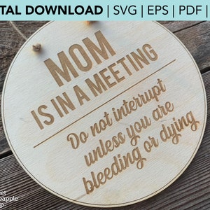 Könnte beinhalten: Ein rundes Schild aus Holz mit dem Text "MOM IS IN A MEETING Do not interrupt unless you are bleeding or dying" in brauner Schrift.