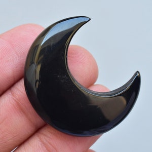 Puede incluir: Un objeto brillante en forma de media luna negra. La luna es lisa y reflectante, con una forma curvada. El objeto es probablemente un artículo decorativo o una joya, posiblemente hecho de piedra pulida o resina.