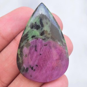 May include: A pear-shaped polished gemstone featuring a vibrant magenta-pink center section contrasted by deep forest green and black mineral inclusions throughout the surface, displaying a smooth, glossy finish and a distinct teardrop silhouette.