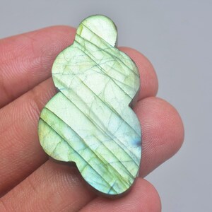 Può includere: Una pietra preziosa di labradorite lucidata con una forma liscia, irregolare e multilobata. La pietra mostra un vibrante riflesso iridescente con lampi di verde lime e blu pallido, accentuati da sottili inclusioni lineari scure sulla superficie.