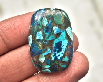 May include: An oval-shaped cabochon gemstone featuring a mosaic pattern of vibrant blue and green stone fragments embedded in a dark matrix with shimmering copper-colored metallic inclusions throughout the polished surface of the stone.