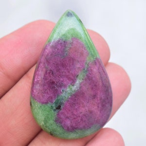 May include: A teardrop-shaped polished gemstone featuring a vibrant magenta-pink center surrounded by a smooth, light green border. The stone displays a natural, mottled texture with distinct color separation between the pink and green sections.