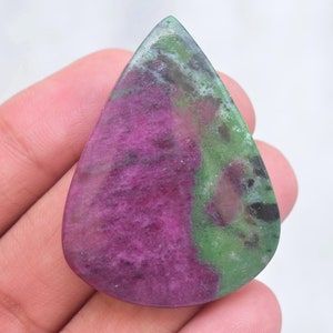 Può includere: Una pietra preziosa lucidata a forma di goccia che presenta un mix vibrante di inclusioni minerali color magenta intenso e verde bosco. La superficie è liscia e lucida, mostrando un contrasto naturale tra le sezioni di pietra rosa scuro e verde.