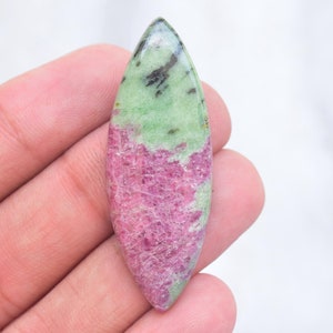May include: A marquise-shaped cabochon gemstone featuring a distinct color split between a vibrant magenta-pink section and a pale mint-green section, with dark inclusions visible within the green portion of the polished stone surface.