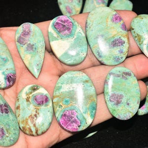 Peut inclure: Une collection de pierres précieuses polies en cabochon présentant un mélange vibrant de pierre matricielle vert menthe et sarcelle avec des inclusions de rubis magenta et fuchsia profond. Ces pierres lisses, arrondies et en forme de goutte.