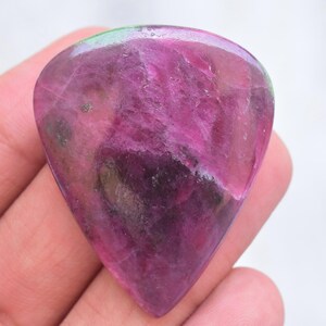 Può includere: Una pietra preziosa lucidata a forma di goccia caratterizzata da una vibrante tavolozza di colori magenta e viola intenso con strutture cristalline interne visibili e una superficie liscia e lucida che riflette la luce.
