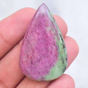 May include: A pear-shaped cabochon gemstone featuring a vibrant magenta-pink center with natural crystalline texture, contrasted by a smooth, opaque light green border with small dark inclusions along the right side and base of the stone.