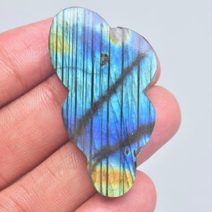 May include: A polished labradorite gemstone with a vibrant blue and yellow iridescent sheen. The stone features a distinct pattern of dark, vertical, and diagonal inclusions running across its surface, creating a textured appearance.