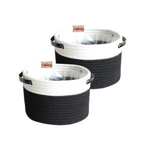 May include: Two round, two-toned rope baskets. The bottom half of each basket is black, and the top half is white. Each basket has black handles and a small brown tag. The baskets are likely for storage or decorative purposes.