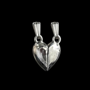 Peut inclure: Un pendentif en métal argenté en forme de cœur divisé en deux moitiés distinctes. Chaque moitié présente une bélière verticale sur le dessus pour la fixation, avec une surface lisse, réfléchissante et polie qui capte la lumière.