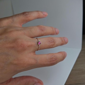 Peut inclure: Une délicate bague en or ornée d'une pierre précieuse rose vif en forme de cœur. La bague a un design simple, avec un fin anneau et un cœur proéminent. La couleur de la pierre précieuse contraste magnifiquement avec l'or.