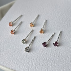 Peut inclure: Un ensemble de sept boucles d'oreilles à tige avec de petites pierres précieuses facettées et multicolores montées sur des tiges en métal argenté. Les pierres présentent des tons orange, ambre, gris et rouge foncé, fixées par des griffes.
