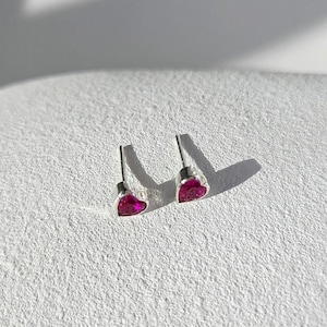Peut inclure: Une paire de boucles d'oreilles à tige avec des pierres en forme de cœur d'un rose fuchsia vif, serties dans un métal argenté brillant. Chaque boucle d'oreille est dotée d'une tige droite, conçue pour les oreilles percées.