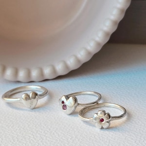Peut inclure: Trois bagues en argent avec des accents de pierres précieuses rouges. Une bague présente une forme de cœur, une autre une forme de cœur et la troisième une forme de fleur.