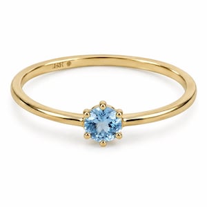Peut inclure: Une bague en or délicate ornée d'une pierre précieuse bleue clair de forme ronde. La bague a un fin anneau et un sertissage à six griffes qui maintient la pierre précieuse. Un bijou classique.