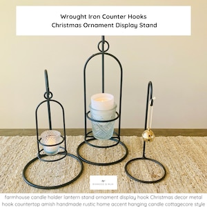 May include: Three black wrought iron display stands. The stands are in the shape of a lantern and a hook. The text on the image reads "Wrought Iron Counter Hooks Christmas Ornament Display Stand".