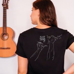 Può includere: Una maglietta nera con una grafica bianca di una persona che arrampica con il testo "Just Send It" sul retro.