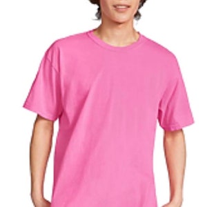 May include: A solid pink t-shirt with short sleeves. The shirt is a vibrant shade of pink and appears to be made of a soft material. The model is wearing blue jeans. The t-shirt has a classic crew neck design.