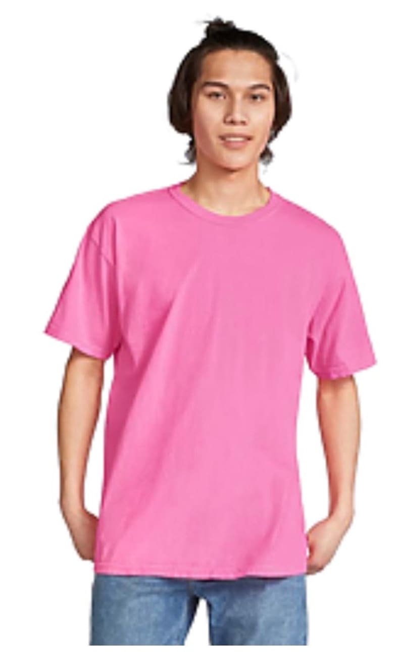 May include: A solid pink t-shirt with short sleeves. The shirt is a vibrant shade of pink and appears to be made of a soft material. The model is wearing blue jeans. The t-shirt has a classic crew neck design.