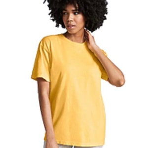 May include: A person wearing a yellow short-sleeved t-shirt and light gray pants. The t-shirt is a solid color and appears to be made of a soft material. The person has dark, curly hair.
