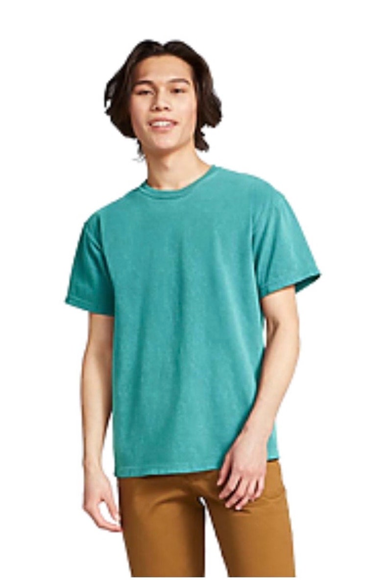 May include: A teal-colored, short-sleeved t-shirt. The shirt has a crew neck and a slightly faded appearance. The person is wearing brown pants. The background is white.