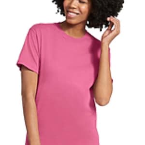 May include: A short-sleeved, solid pink t-shirt. The shirt is made of a soft material and is worn with light blue jeans. The person in the image has dark, curly hair.