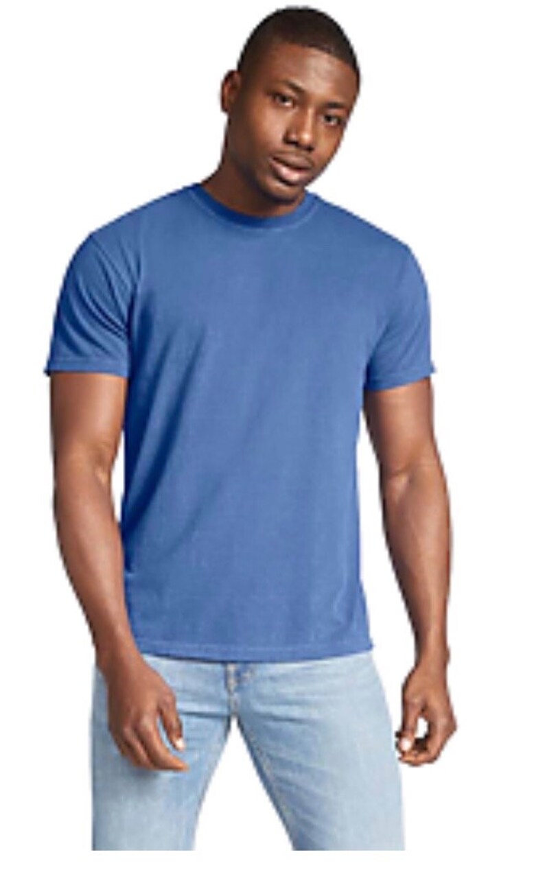 May include: A solid blue t-shirt with short sleeves. The shirt is made of a soft material and is paired with light blue jeans. The model is standing in front of a white background.