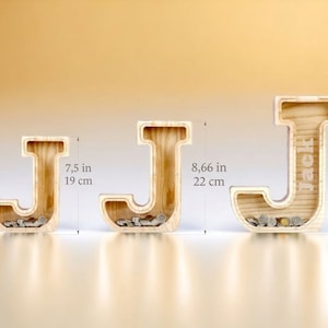 K&ouml;nnte beinhalten: Drei h&ouml;lzerne Sparschweine in Form des Buchstabens J, in verschiedenen Gr&ouml;&szlig;en. Das kleinste ist 19 cm hoch, das mittlere 22 cm und das gr&ouml;&szlig;te 27 cm. Jedes Sparschwein hat einen Schlitz f&uuml;r M&uuml;nzen und ist mit M&uuml;nzen gef&uuml;llt.