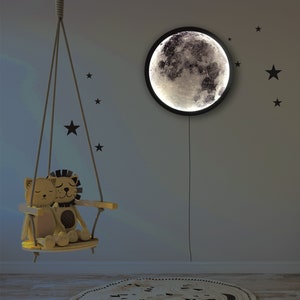 May include: A wooden swing with two plush lion toys sitting on it. The swing is hanging from the ceiling in a room with a moon-shaped nightlight on the wall. The wall is decorated with black star stickers.