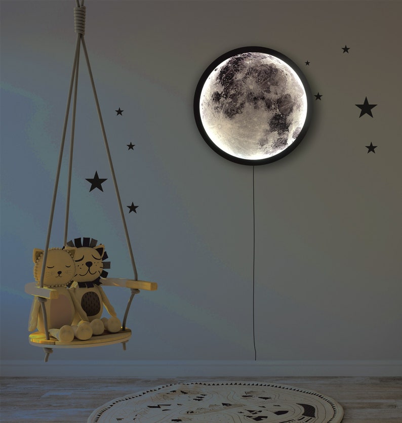 May include: A wooden swing with two plush lion toys sitting on it. The swing is hanging from the ceiling in a room with a moon-shaped nightlight on the wall. The wall is decorated with black star stickers.
