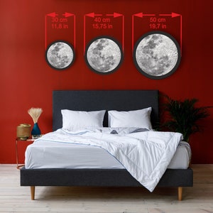 May include: Three round moon-shaped LED lights in different sizes, 11.8 inches, 15.75 inches, and 19.7 inches, hanging on a red wall above a gray bed with white bedding.