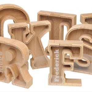 May include: Wooden alphabet letter piggy banks with clear plastic windows. The letters are R, I, D, G, E, F, R, E, D, E, R, I, C, K.