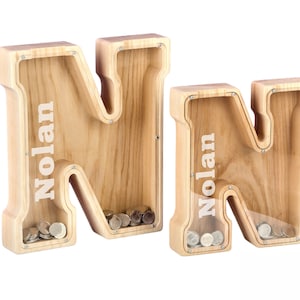 May include: Two wooden money boxes shaped like the letter N. Each box has the name Nolan engraved on the front. The boxes are filled with coins.