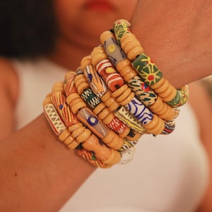 Puede incluir: Un conjunto de pulseras de cuentas coloridas. Las pulseras presentan una variedad de patrones y colores, incluyendo rojo, azul, verde y amarillo. Las cuentas están ensartadas en un cordón beige, creando un accesorio único y llamativo.