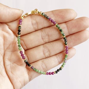 Puede incluir: Un brazalete de cuentas multicolores con cuentas rosas, verdes y negras. El brazalete tiene un cierre dorado.