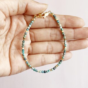 May include: A delicate gold bracelet featuring small turquoise and gold beads. The bracelet is strung on a thin gold chain.