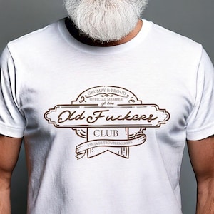 May include: White t-shirt with a brown graphic design that says "Grumpy & Proud, Official Member of the Old Fuckers Club, Vintage Troublemakers".