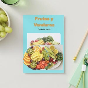 Puede incluir: Un libro para colorear azul claro titulado "Frutas y Verduras" con una colorida ilustración de frutas y verduras. Un cuenco de uvas verdes, un lápiz y un pequeño cuaderno con llaves también son visibles.