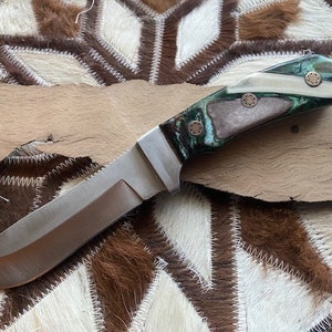 May include: A hunting knife with a stainless steel blade and a green, white, and brown handle with copper accents.