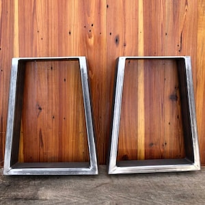 May include: Two silver metal table legs with a trapezoidal shape. The legs are made of sturdy metal and have a brushed finish.