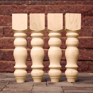 May include: Four unfinished wooden table legs with a turned design. The legs are made of maple wood and have a natural finish.