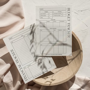 May include: Two printable budget tracker sheets with black text on white paper. The top sheet is labeled "Budget Tracker" and the bottom sheet is labeled "Financial Tracker". Both sheets have sections for income, expenses, and savings.