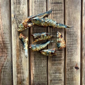 May include: Dried fish arranged in a square shape on a wooden surface. The fish are brown and gray with some white parts.