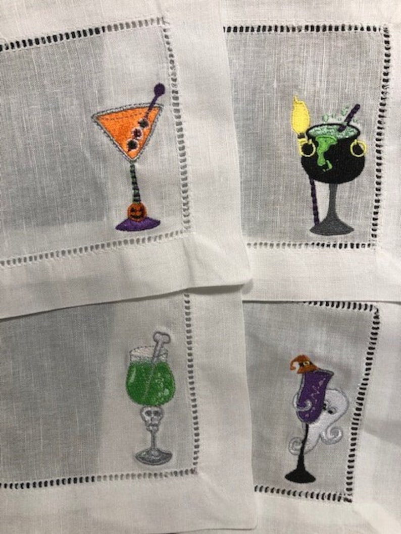 May include: White linen cocktail napkins with embroidered Halloween-themed designs. Each napkin features a different cocktail glass with festive details, including an orange martini, a bubbling cauldron, and a green drink.