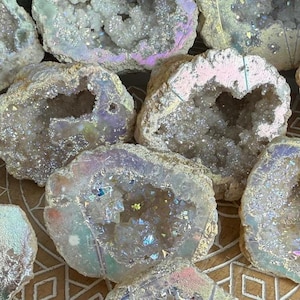 May include: A collection of iridescent white agate geode slices with a variety of shapes and sizes. The geode slices are arranged on a wooden surface with a decorative pattern.