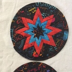 Könnte beinhalten: Zwei schwarze Stoffkreise mit bunten Designs. Der erste Kreis hat einen roten und blauen Stern mit schwarzer Mitte. Der zweite Kreis hat ein buntes Design mit den Worten "He His She" und "God Bless You" in einer kursivschrift.
